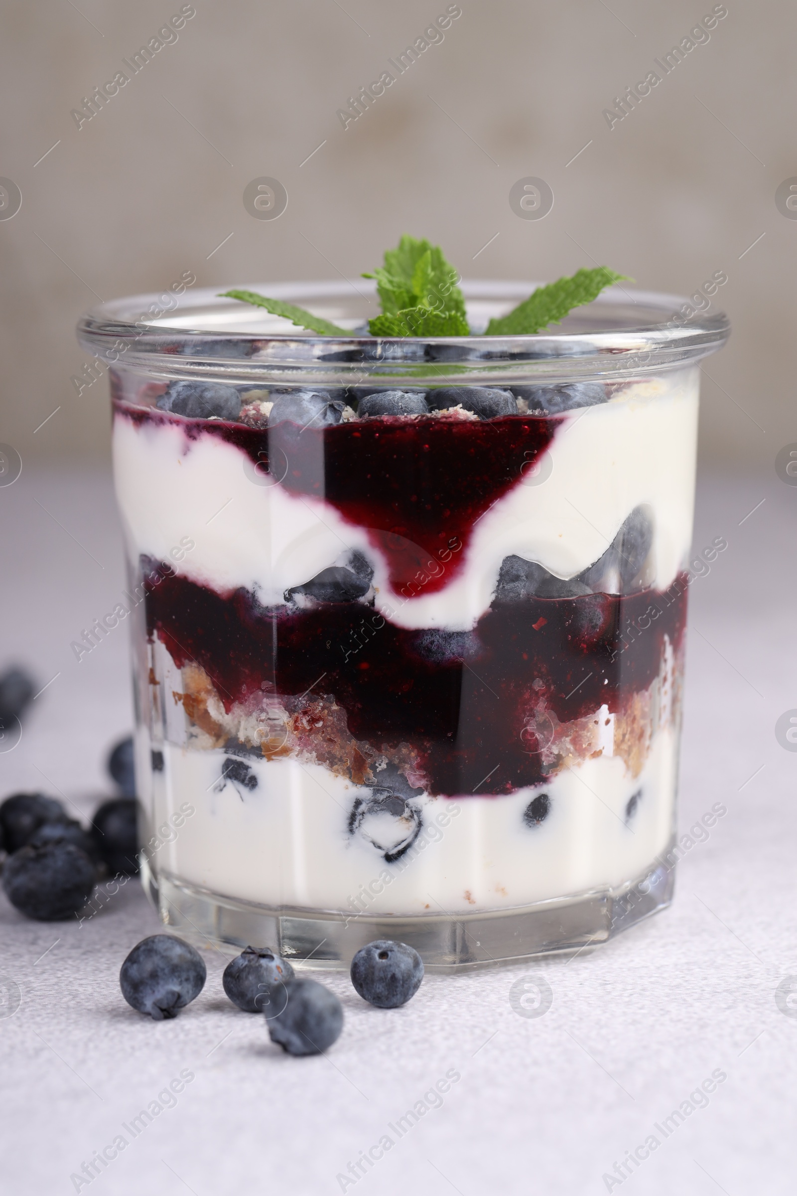 Photo of Tasty trifle dessert. Blueberries, sponge cake and whipped cream in glass on light grey table