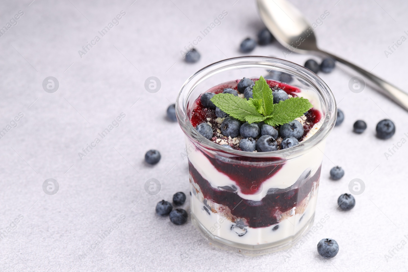 Photo of Tasty trifle dessert. Blueberries, sponge cake and whipped cream in glass on light grey table, space for text