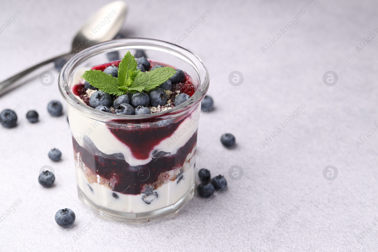 Photo of Tasty trifle dessert. Blueberries, sponge cake and whipped cream in glass on light grey table, space for text