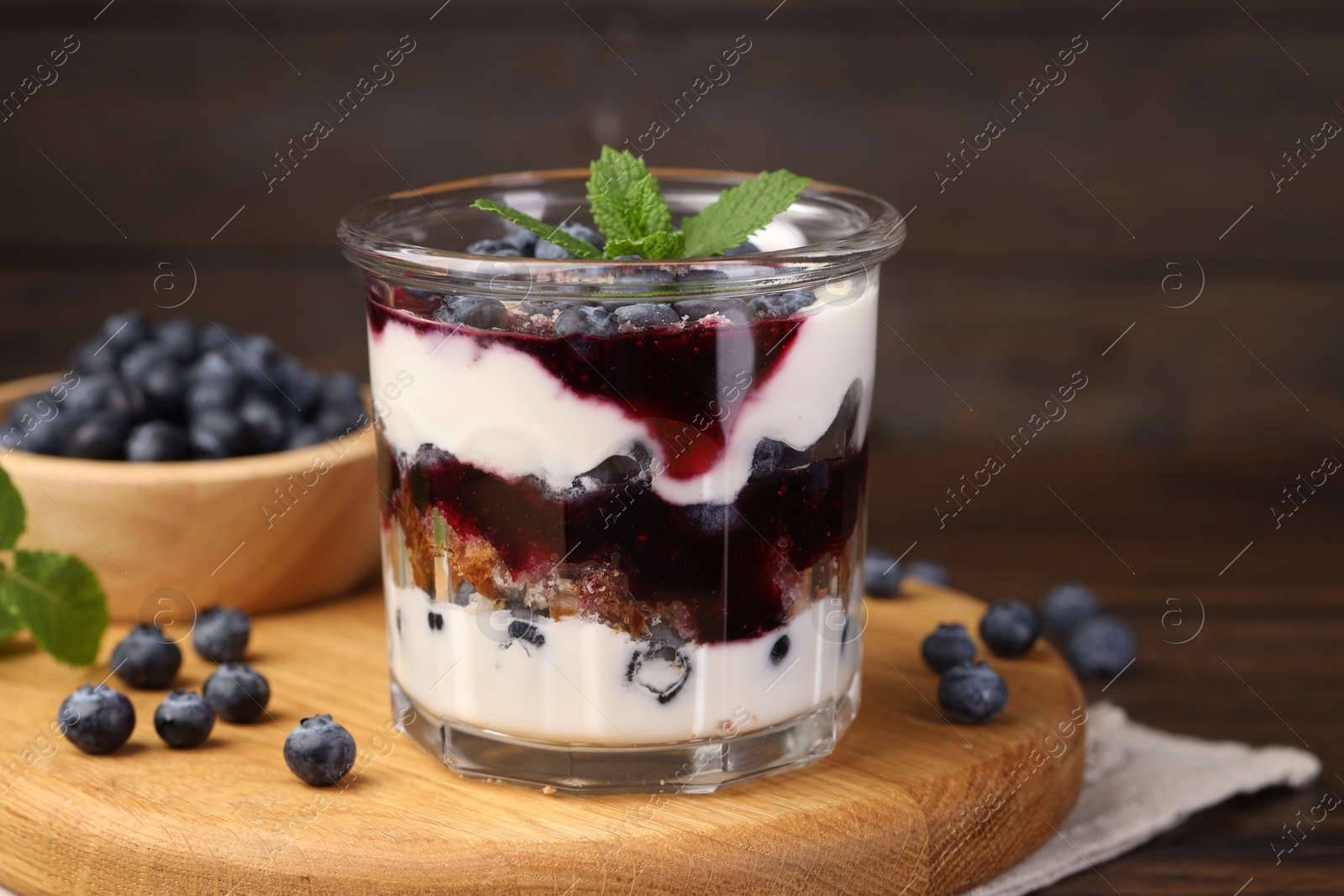 Photo of Tasty trifle dessert. Blueberries, sponge cake and whipped cream in glass on wooden table