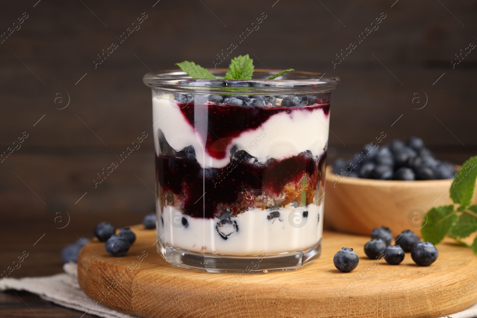 Photo of Tasty trifle dessert. Blueberries, sponge cake and whipped cream in glass on wooden table