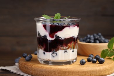 Photo of Tasty trifle dessert. Blueberries, sponge cake and whipped cream in glass on wooden table