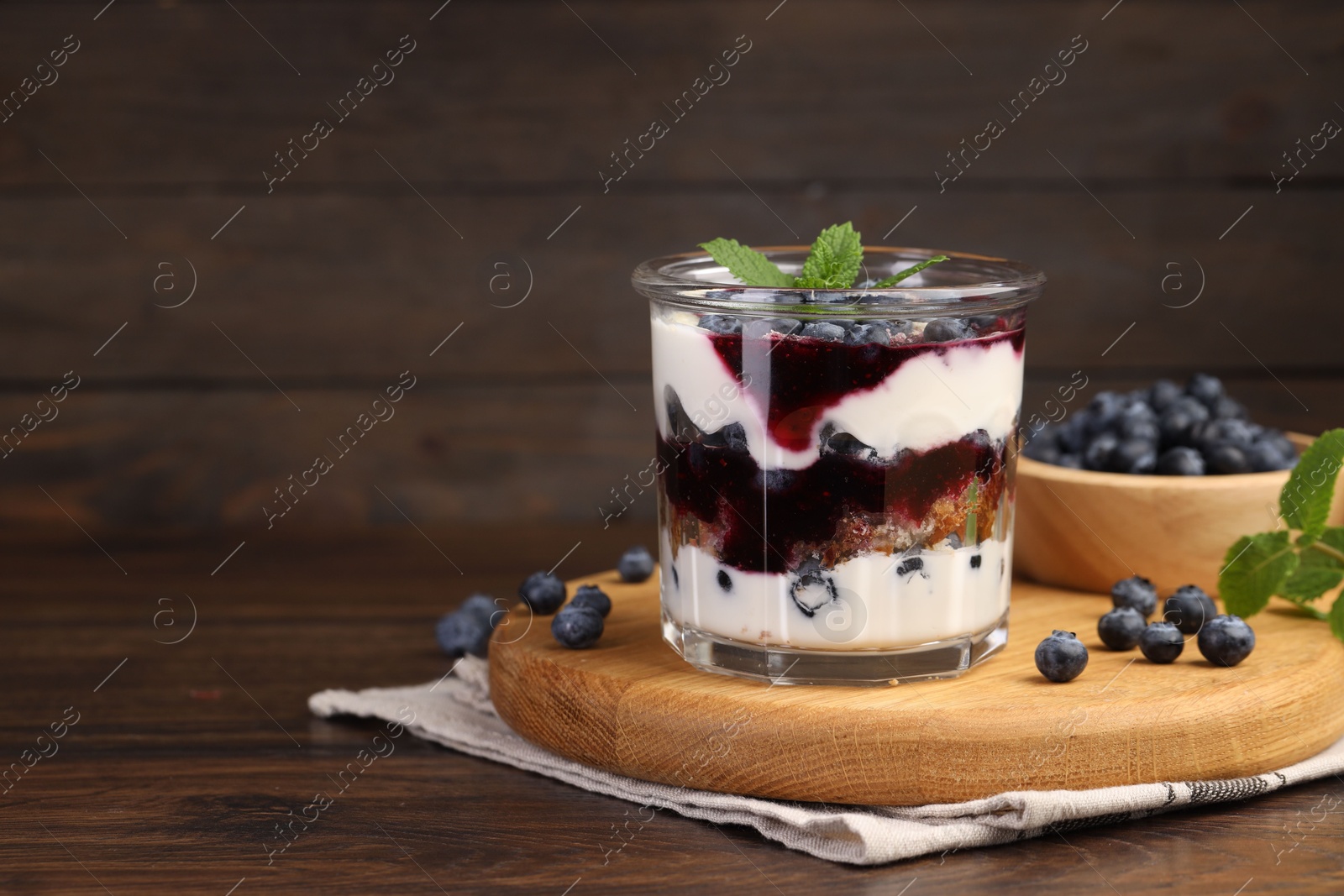 Photo of Tasty trifle dessert. Blueberries, sponge cake and whipped cream in glass on wooden table, space for text