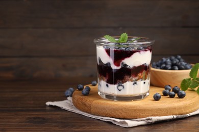 Photo of Tasty trifle dessert. Blueberries, sponge cake and whipped cream in glass on wooden table, space for text