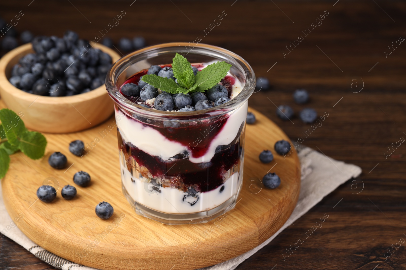 Photo of Tasty trifle dessert. Blueberries, sponge cake and whipped cream in glass on wooden table