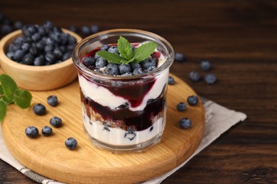 Photo of Tasty trifle dessert. Blueberries, sponge cake and whipped cream in glass on wooden table