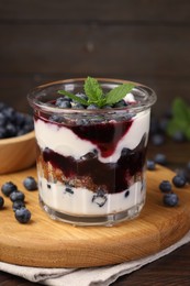 Photo of Tasty trifle dessert. Blueberries, sponge cake and whipped cream in glass on wooden table