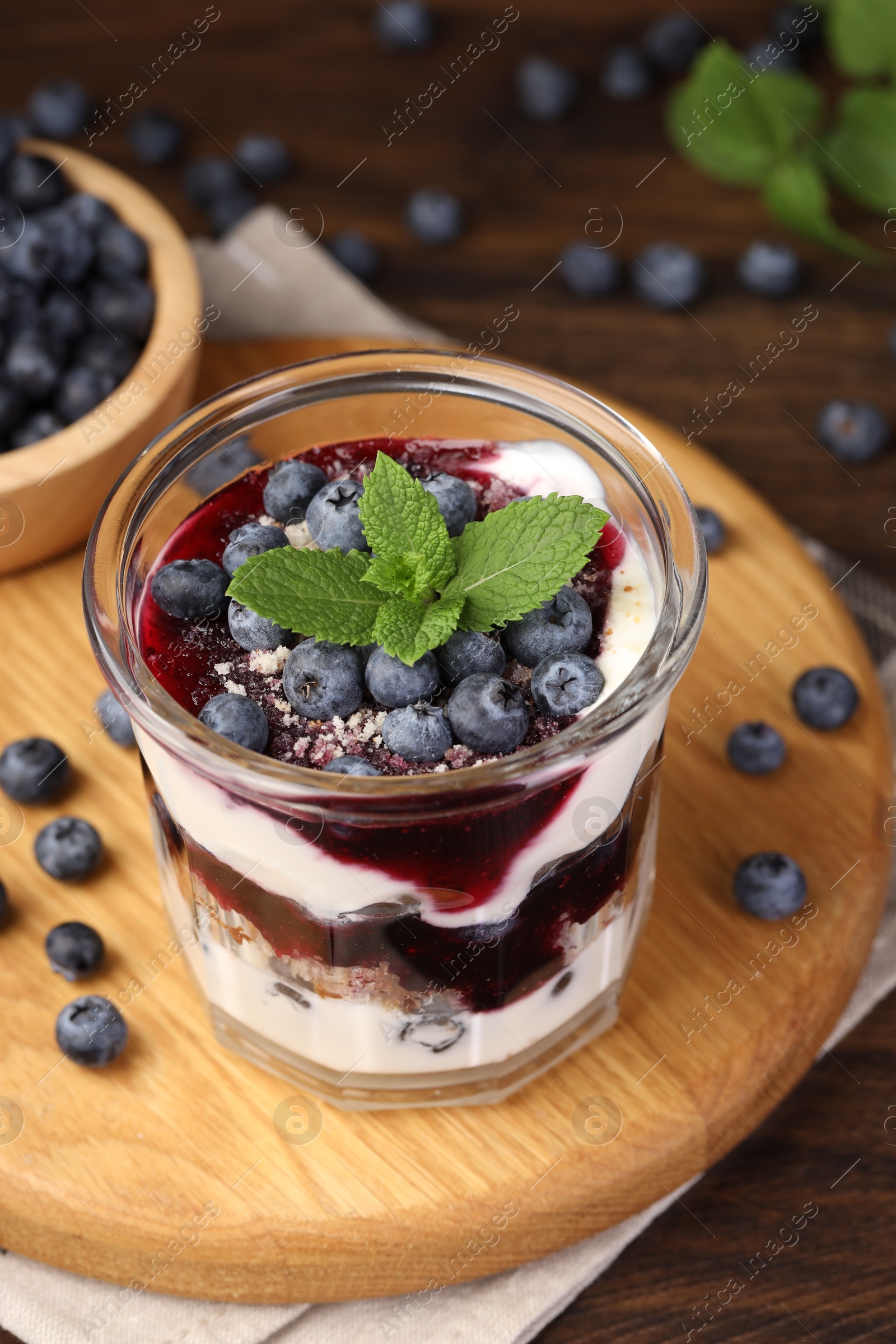 Photo of Tasty trifle dessert. Blueberries, sponge cake and whipped cream in glass on wooden table