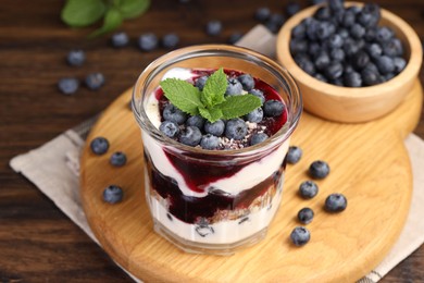 Photo of Tasty trifle dessert. Blueberries, sponge cake and whipped cream in glass on wooden table