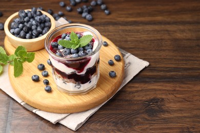 Photo of Tasty trifle dessert. Blueberries, sponge cake and whipped cream in glass on wooden table, space for text