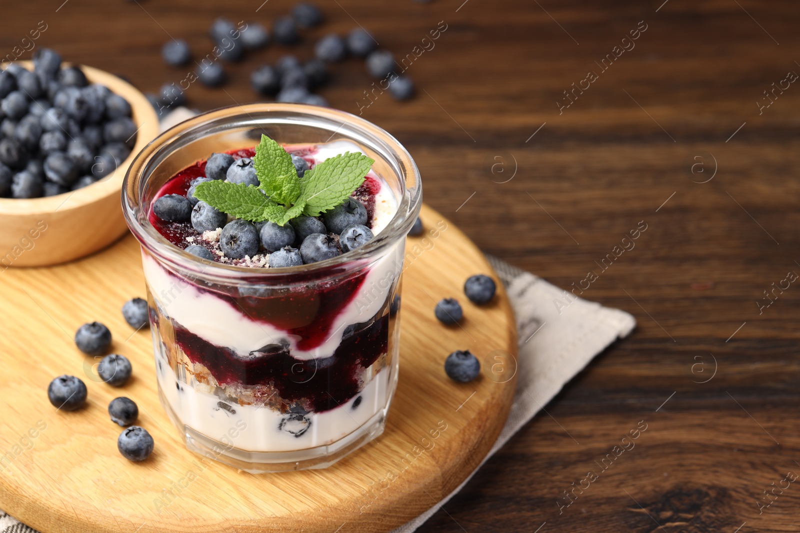 Photo of Tasty trifle dessert. Blueberries, sponge cake and whipped cream in glass on wooden table, space for text