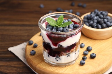 Photo of Tasty trifle dessert. Blueberries, sponge cake and whipped cream in glass on wooden table