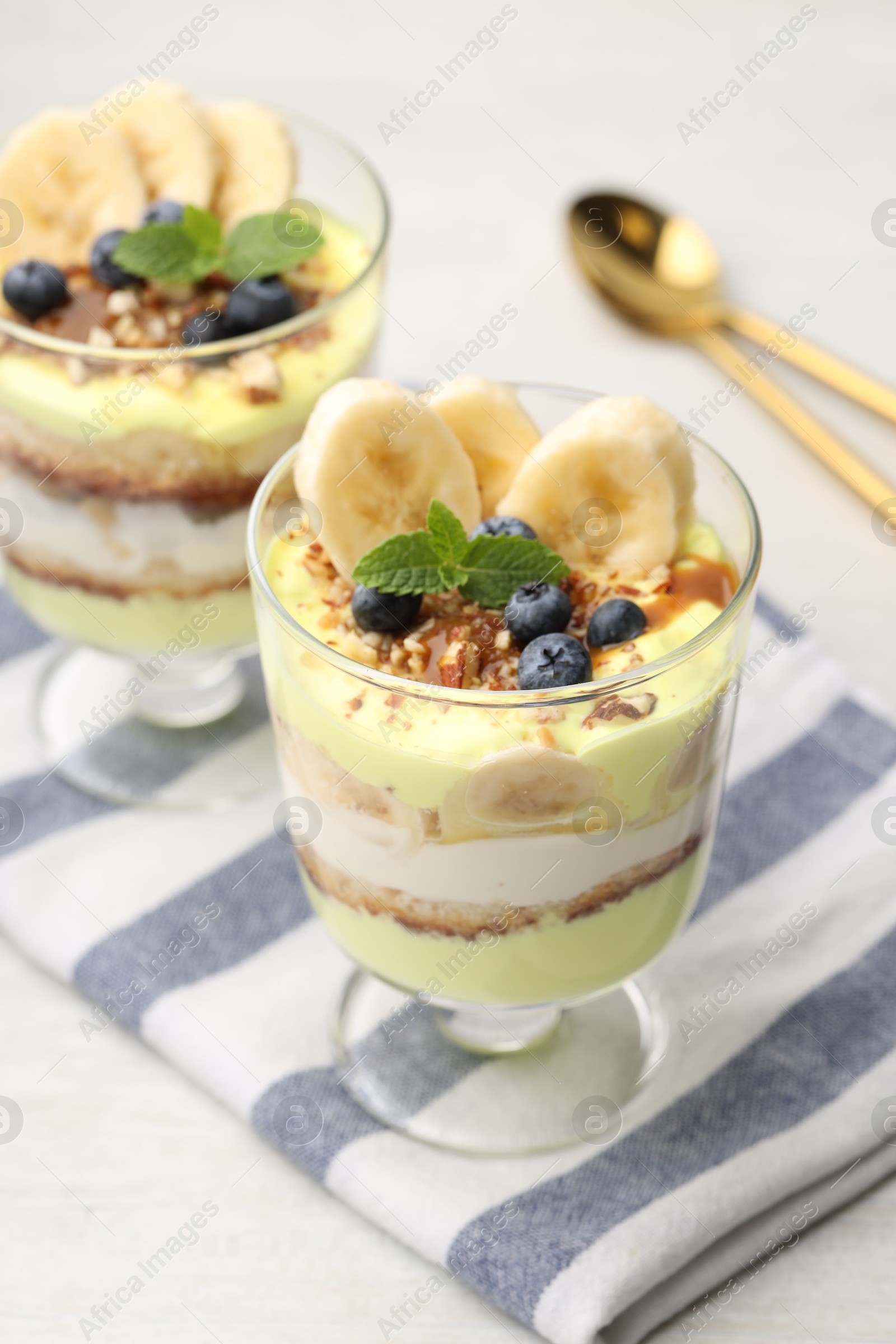 Photo of Tasty trifle dessert. Banana, blueberries, sponge cake and whipped cream in glasses on white wooden table