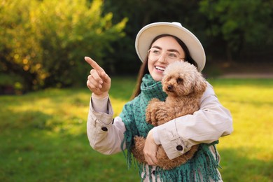 Smiling woman pointing at something to cute dog in autumn park