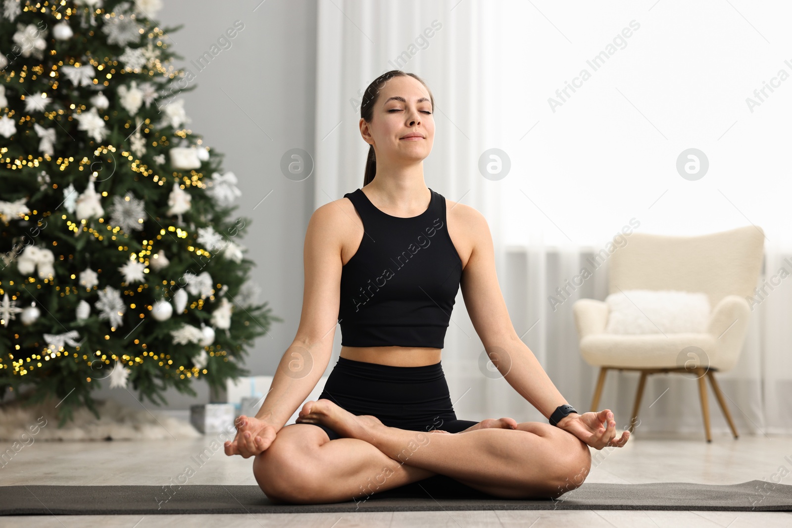 Photo of Woman practicing yoga against Christmas tree indoors