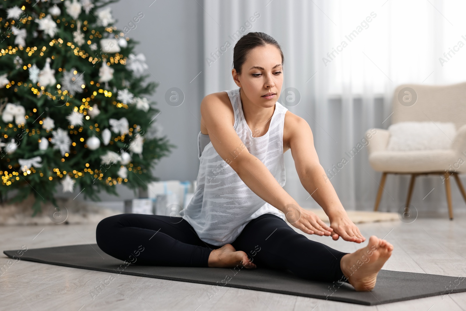 Photo of Woman practicing yoga against Christmas tree indoors