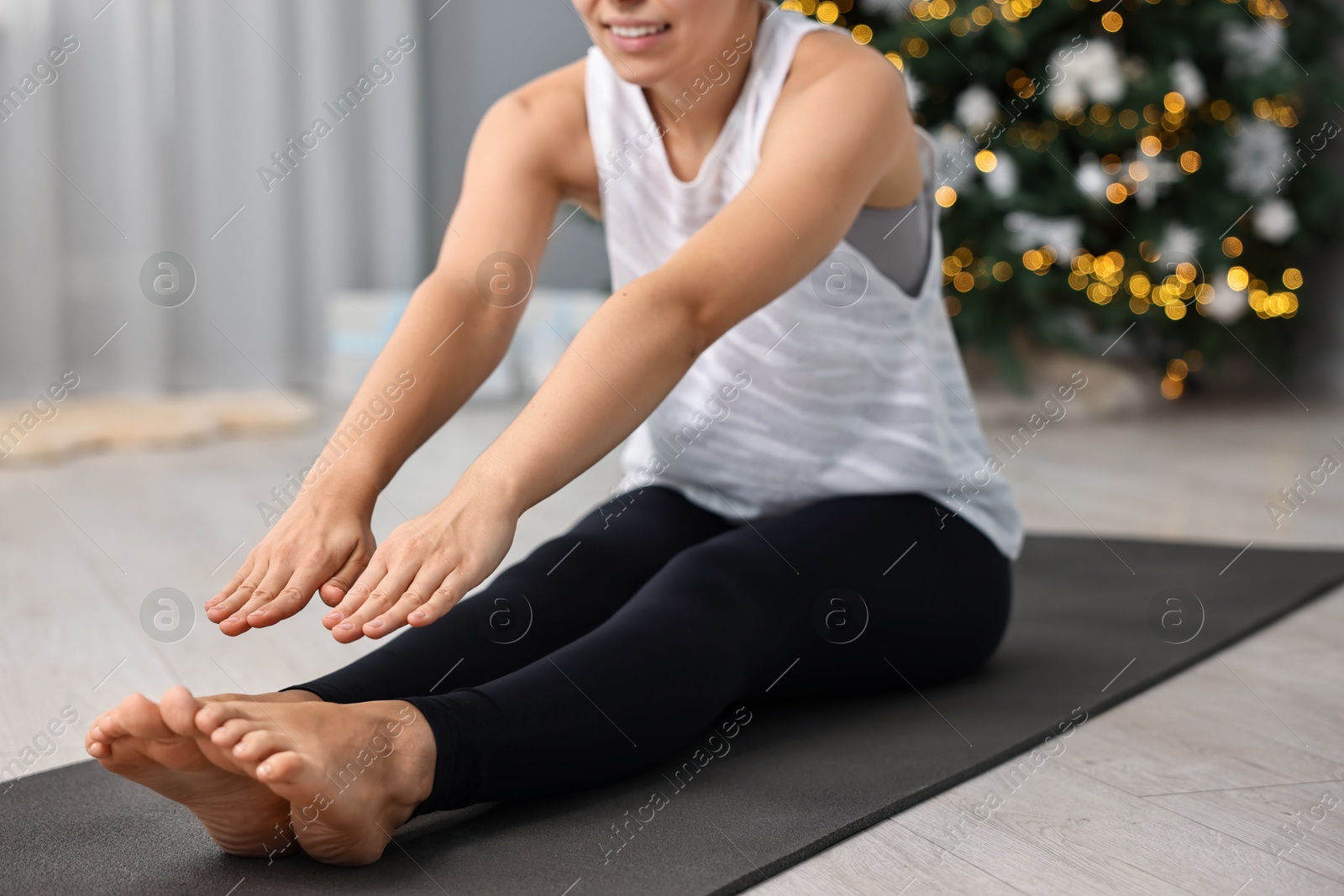 Photo of Woman practicing yoga against blurred Christmas lights indoors, closeup