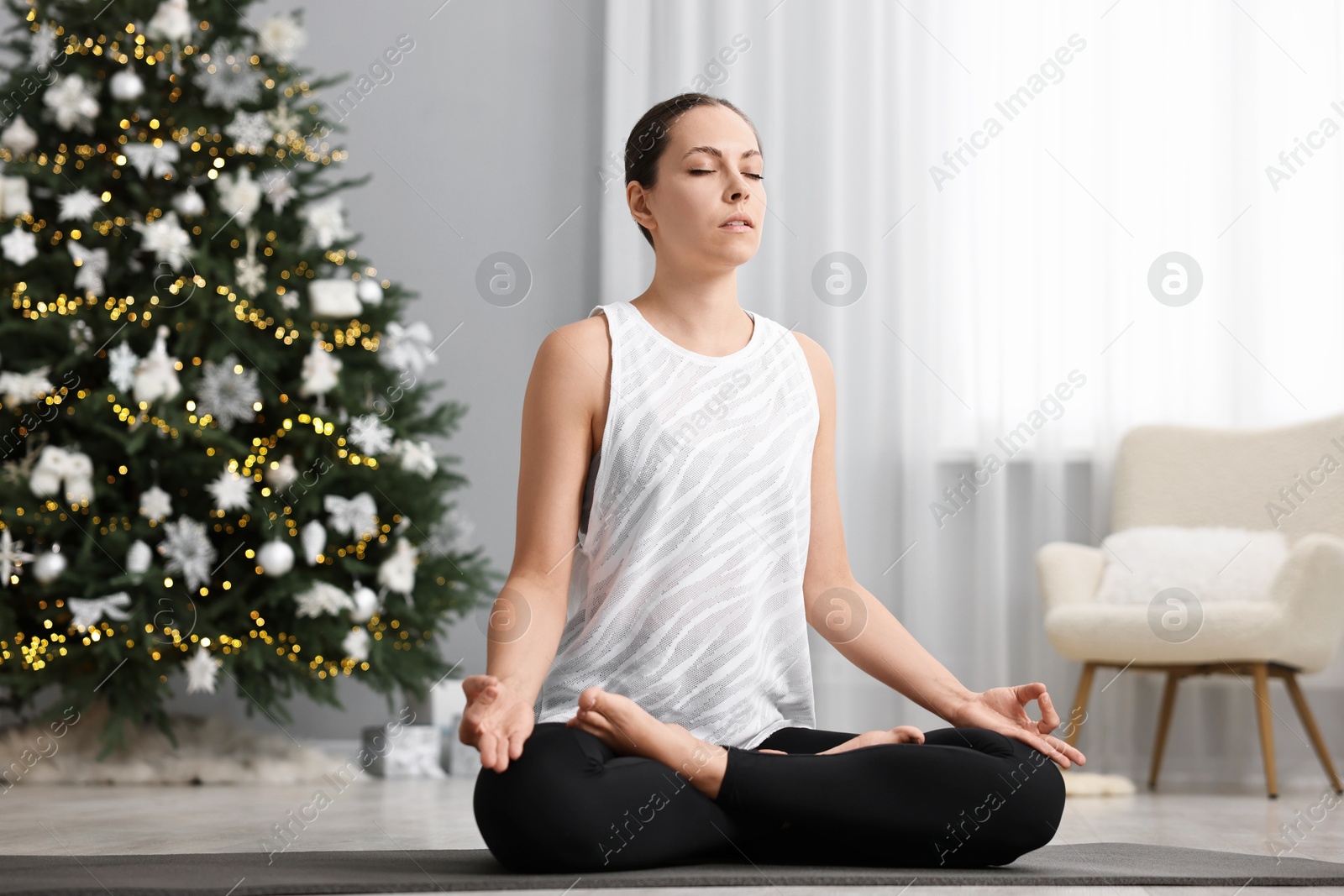 Photo of Woman practicing yoga against Christmas tree indoors