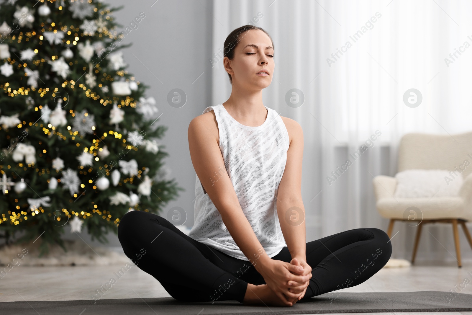 Photo of Woman practicing yoga against Christmas tree indoors