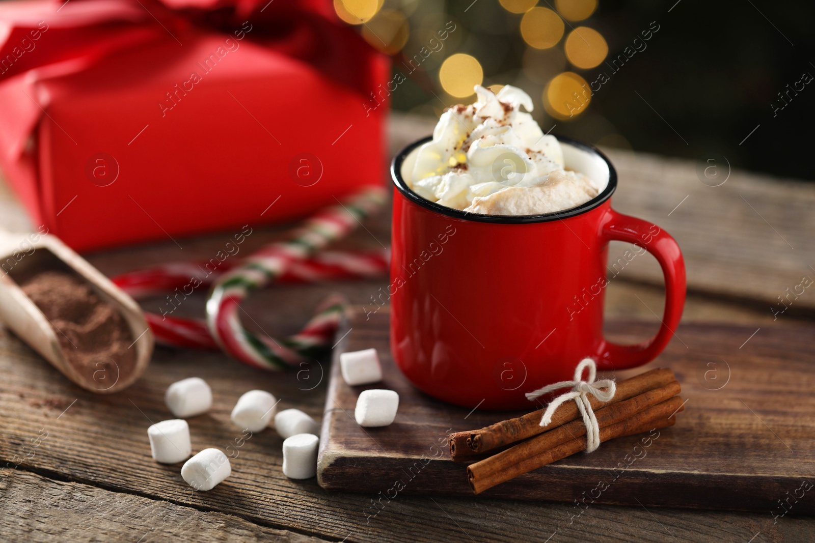 Photo of Tasty hot cocoa drink with whipped cream in mug, marshmallows and spices on wooden table