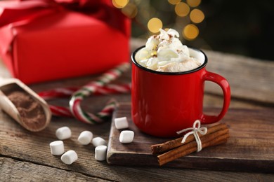 Photo of Tasty hot cocoa drink with whipped cream in mug, marshmallows and spices on wooden table