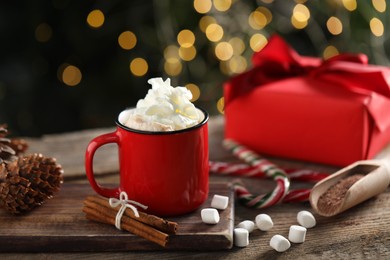 Photo of Tasty hot cocoa drink with whipped cream in mug, marshmallows and spices on wooden table