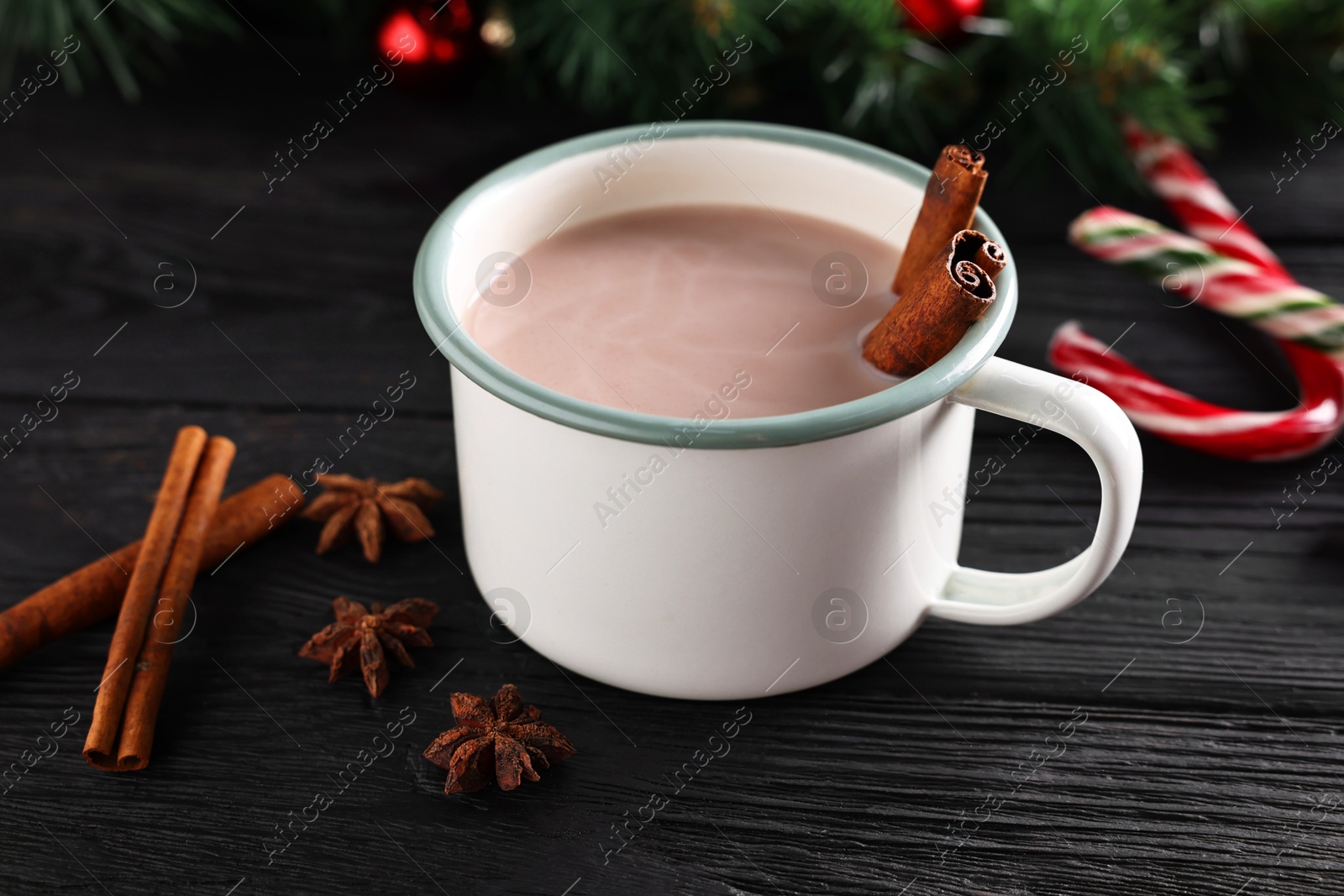 Photo of Tasty hot cocoa drink in mug and spices on black wooden table, closeup