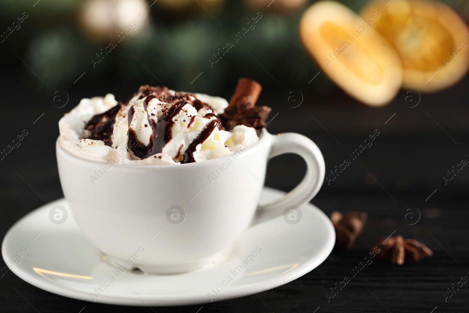 Photo of Tasty hot cocoa drink with whipped cream in cup and spices on black table, closeup