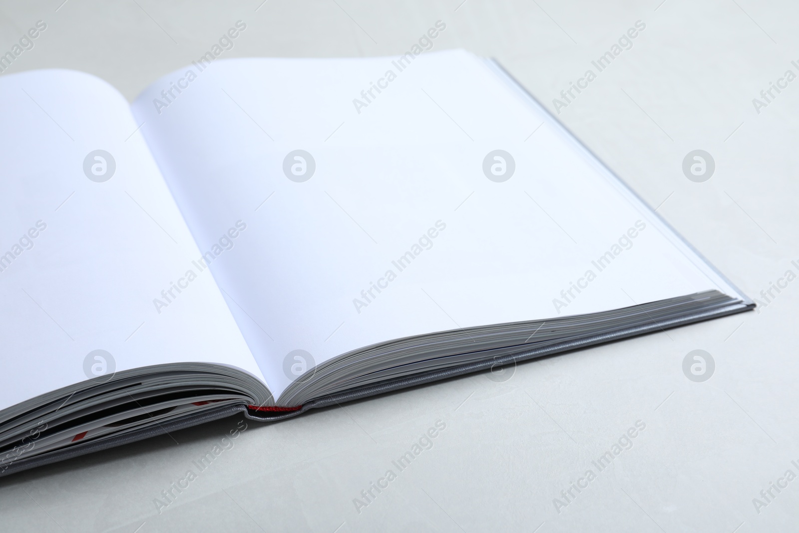 Photo of Open book with hard cover on light grey table, closeup