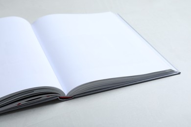 Photo of Open book with hard cover on light grey table, closeup