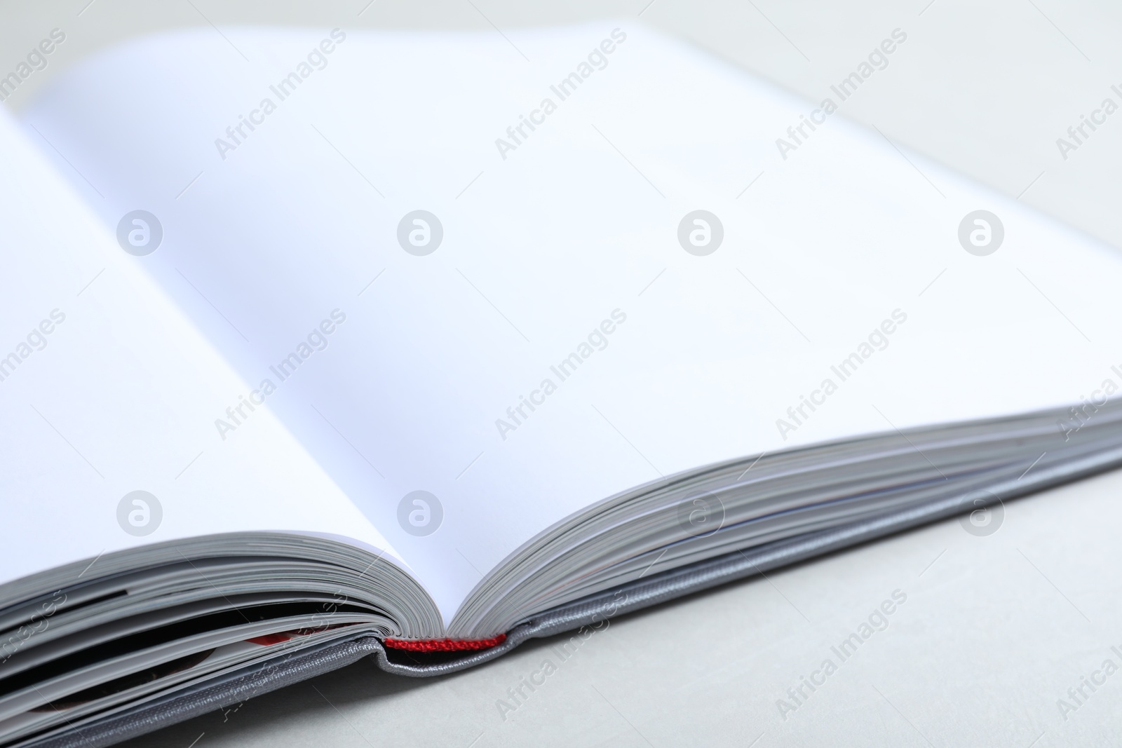 Photo of Open book with hard cover on light grey table, closeup