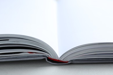 Photo of Open book with hard cover on light grey table, closeup