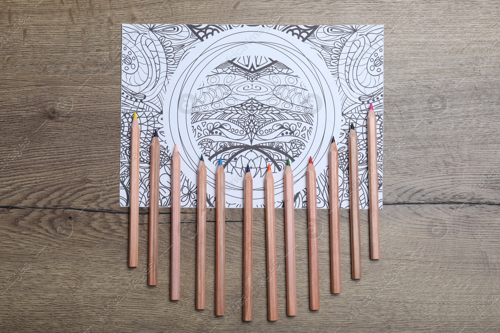 Photo of Antistress coloring page and pencils on wooden table, flat lay