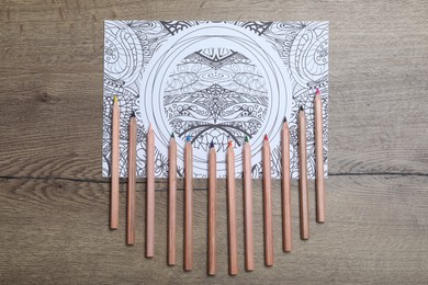 Photo of Antistress coloring page and pencils on wooden table, flat lay