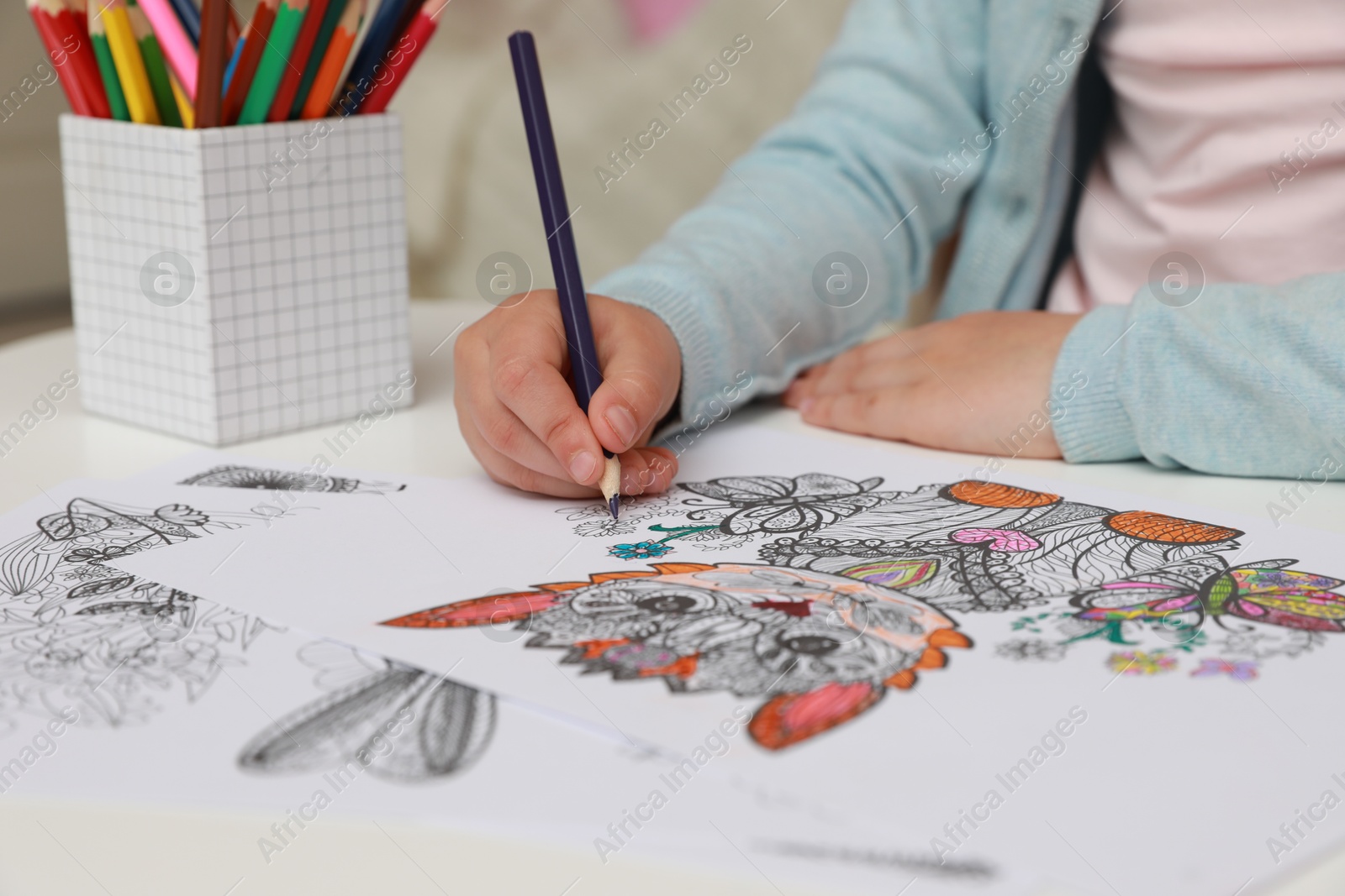 Photo of Little girl coloring antistress page at table, closeup