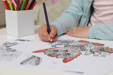 Photo of Little girl coloring antistress page at table, closeup