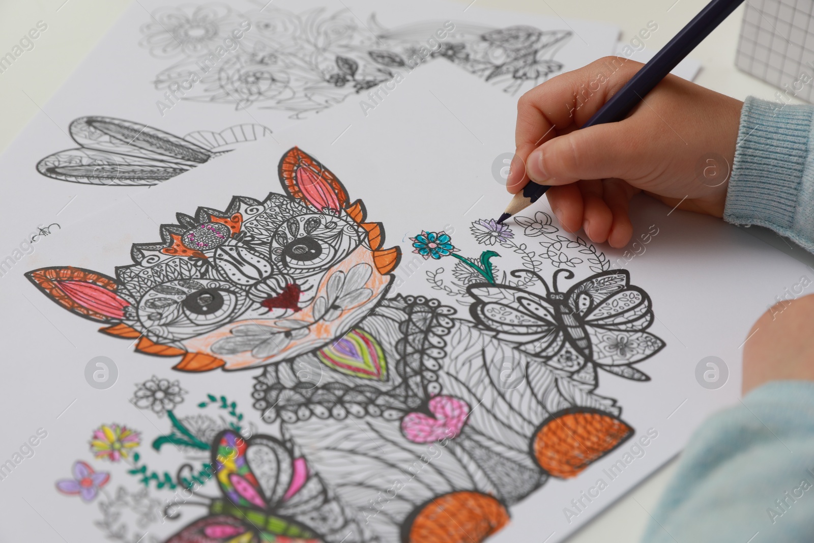 Photo of Little girl coloring antistress page at table, closeup