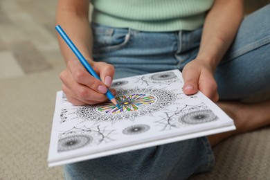 Young woman coloring antistress page on floor, closeup