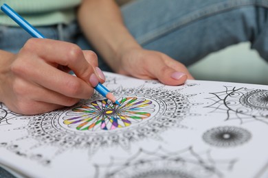 Photo of Young woman coloring antistress page on blurred background, closeup