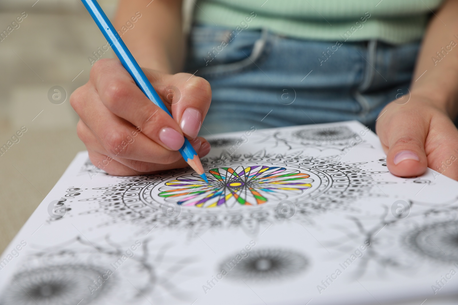 Photo of Young woman coloring antistress page on blurred background, closeup