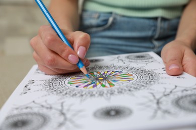 Photo of Young woman coloring antistress page on blurred background, closeup