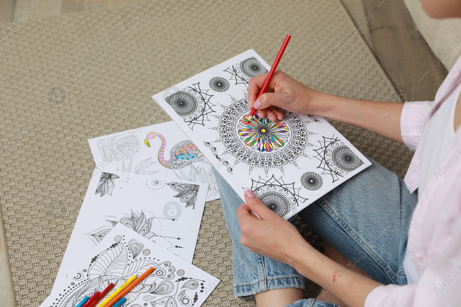 Photo of Young woman coloring antistress page on floor, closeup