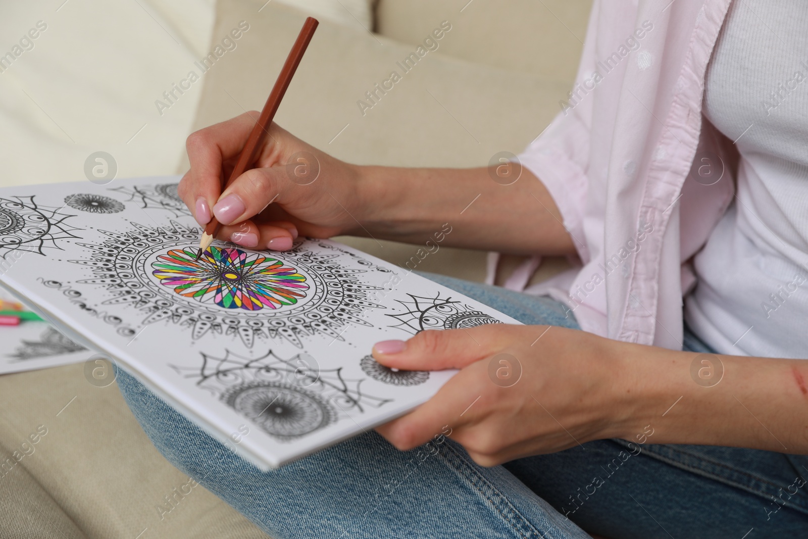 Photo of Young woman coloring antistress page on sofa, closeup