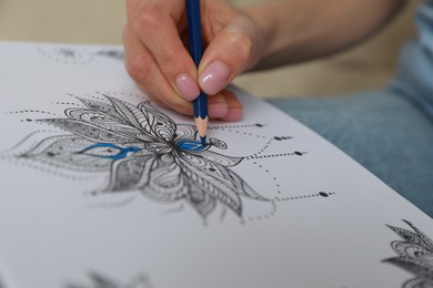 Photo of Young woman coloring antistress page on blurred background, closeup