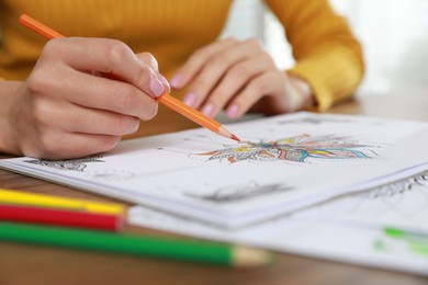 Young woman coloring antistress page at table indoors, closeup