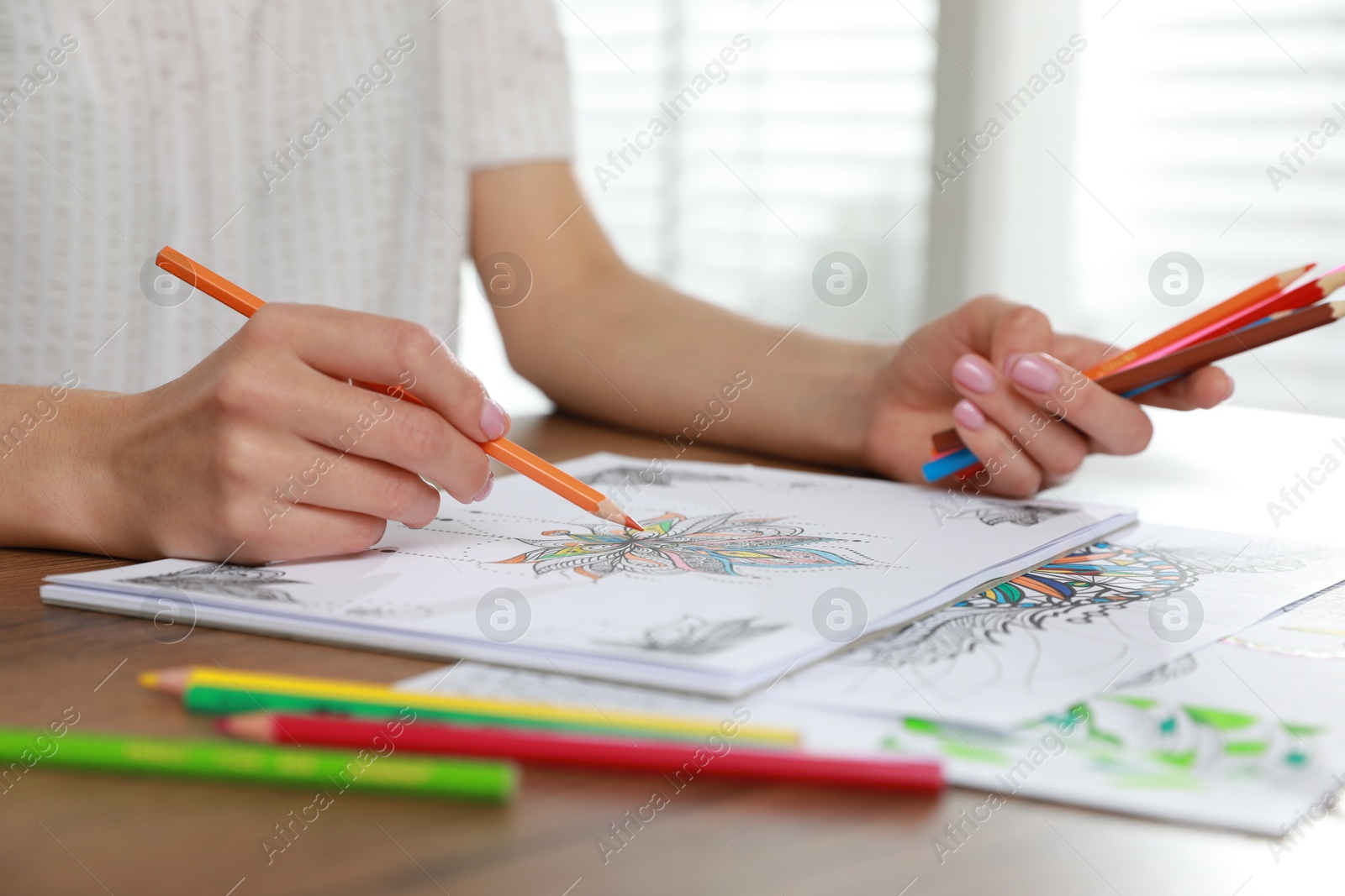 Photo of Young woman coloring antistress page at table indoors, closeup