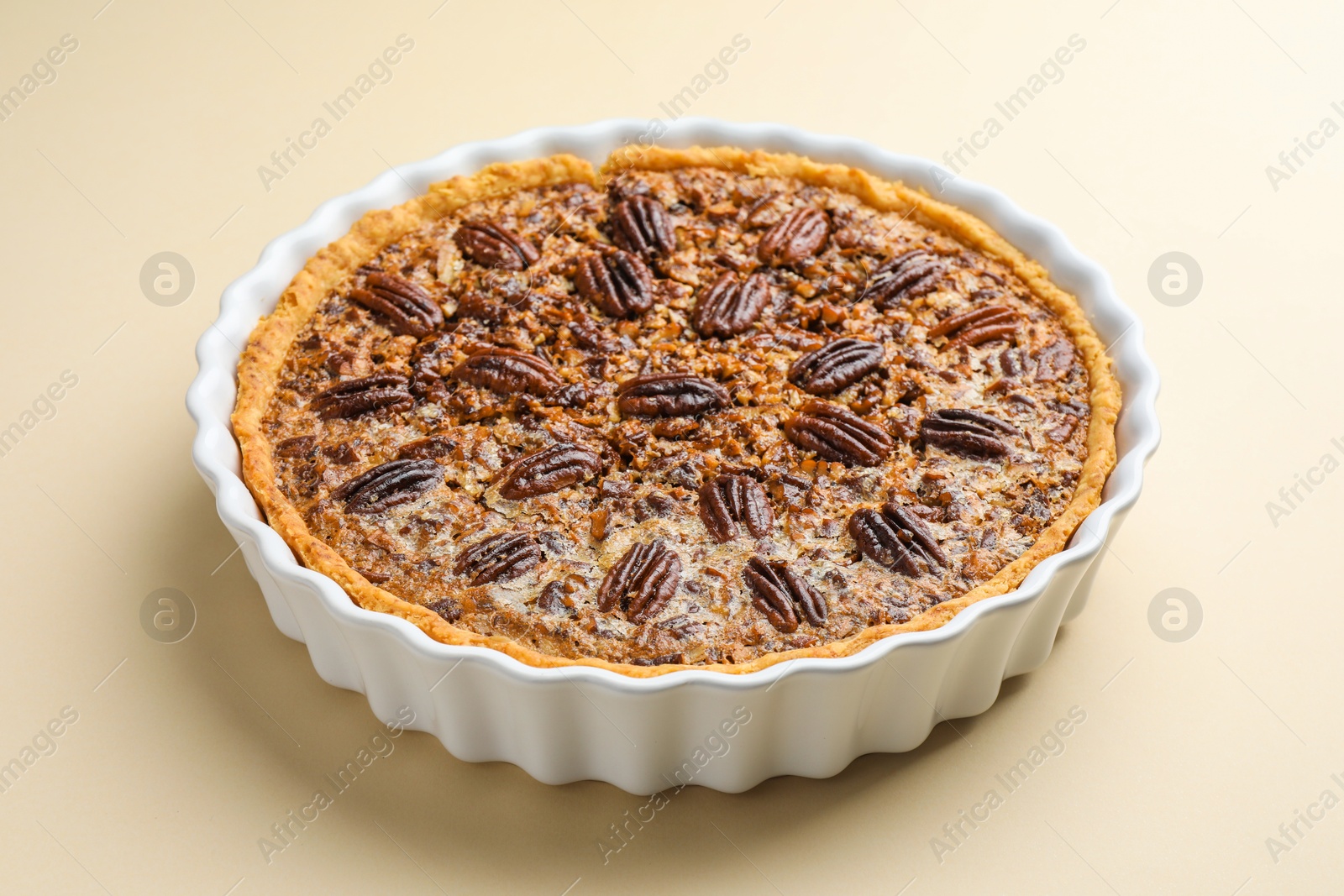 Photo of Delicious pecan pie in baking dish on beige background, closeup