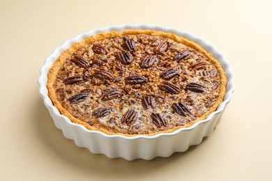 Photo of Delicious pecan pie in baking dish on beige background, closeup