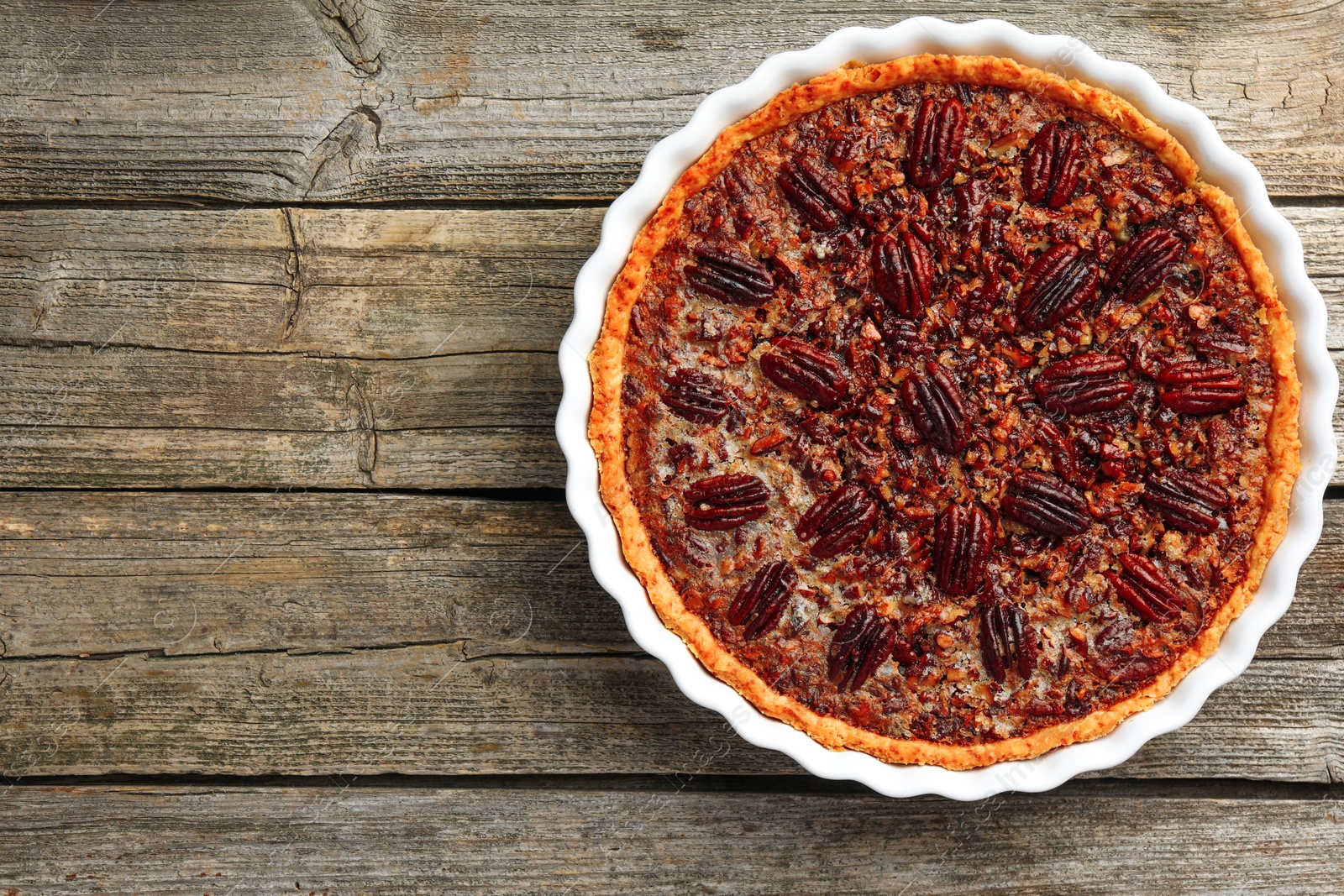 Photo of Delicious pecan pie in baking dish on wooden table, top view. Space for text