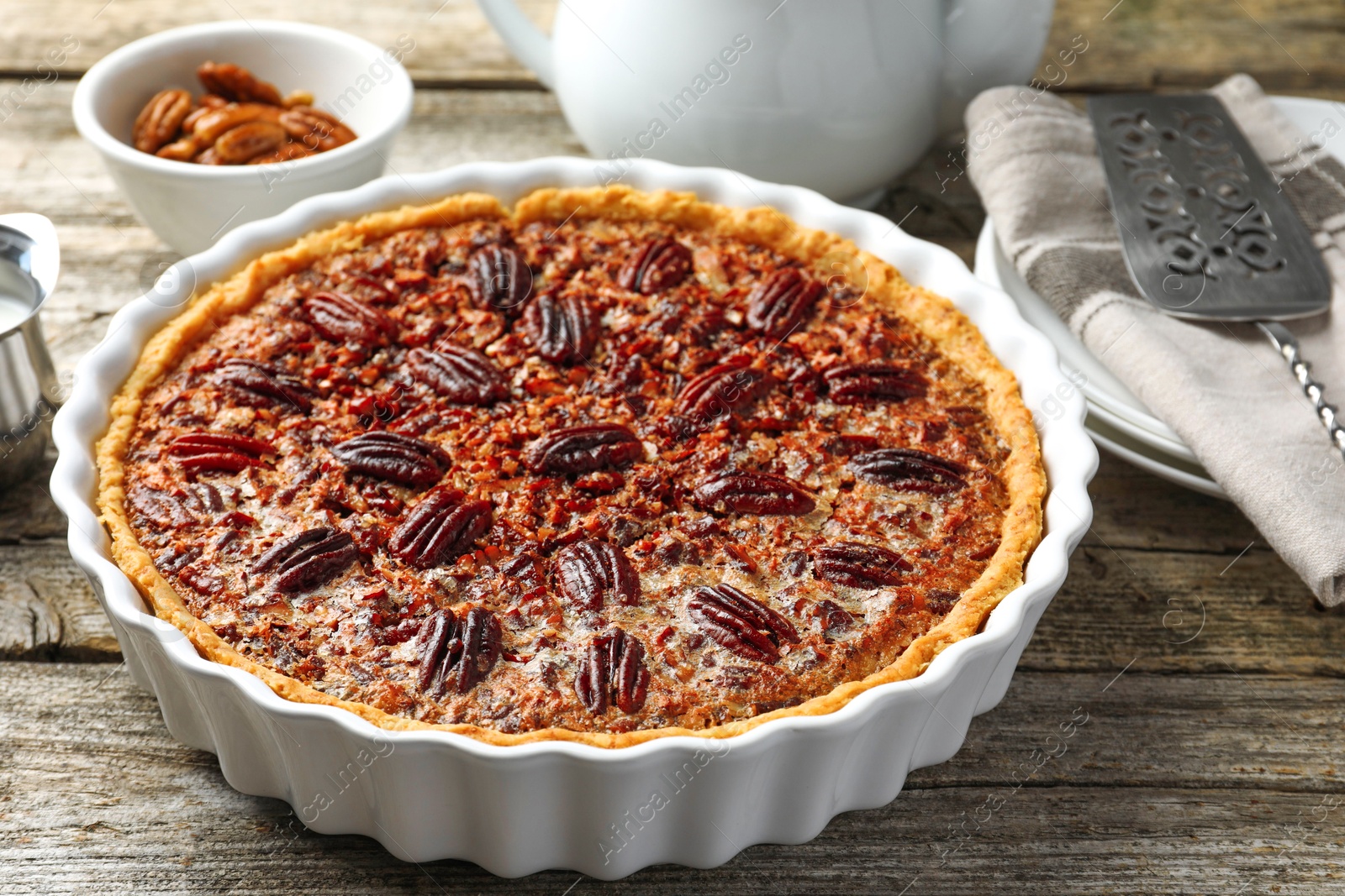 Photo of Delicious pecan pie in baking dish on wooden table, closeup